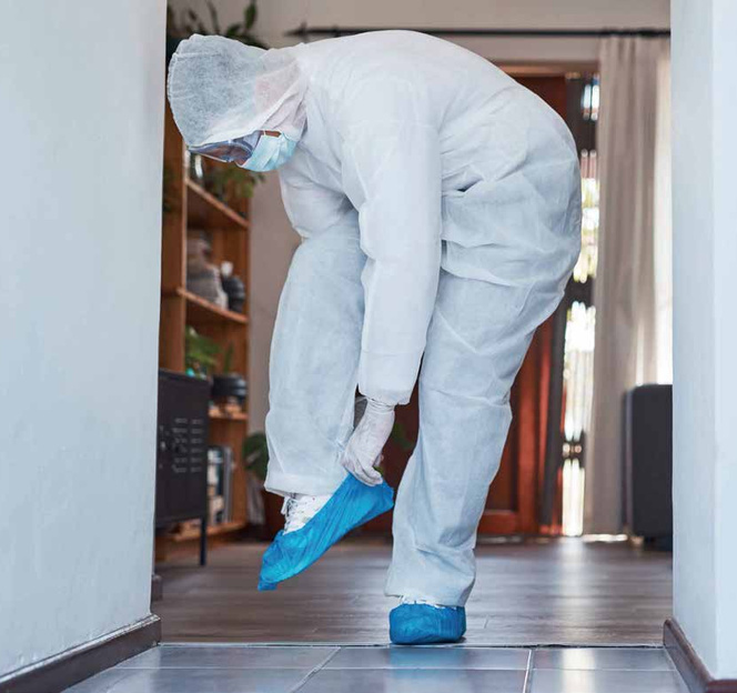 Personne en combinaison de protection mettant des surchaussures bleues